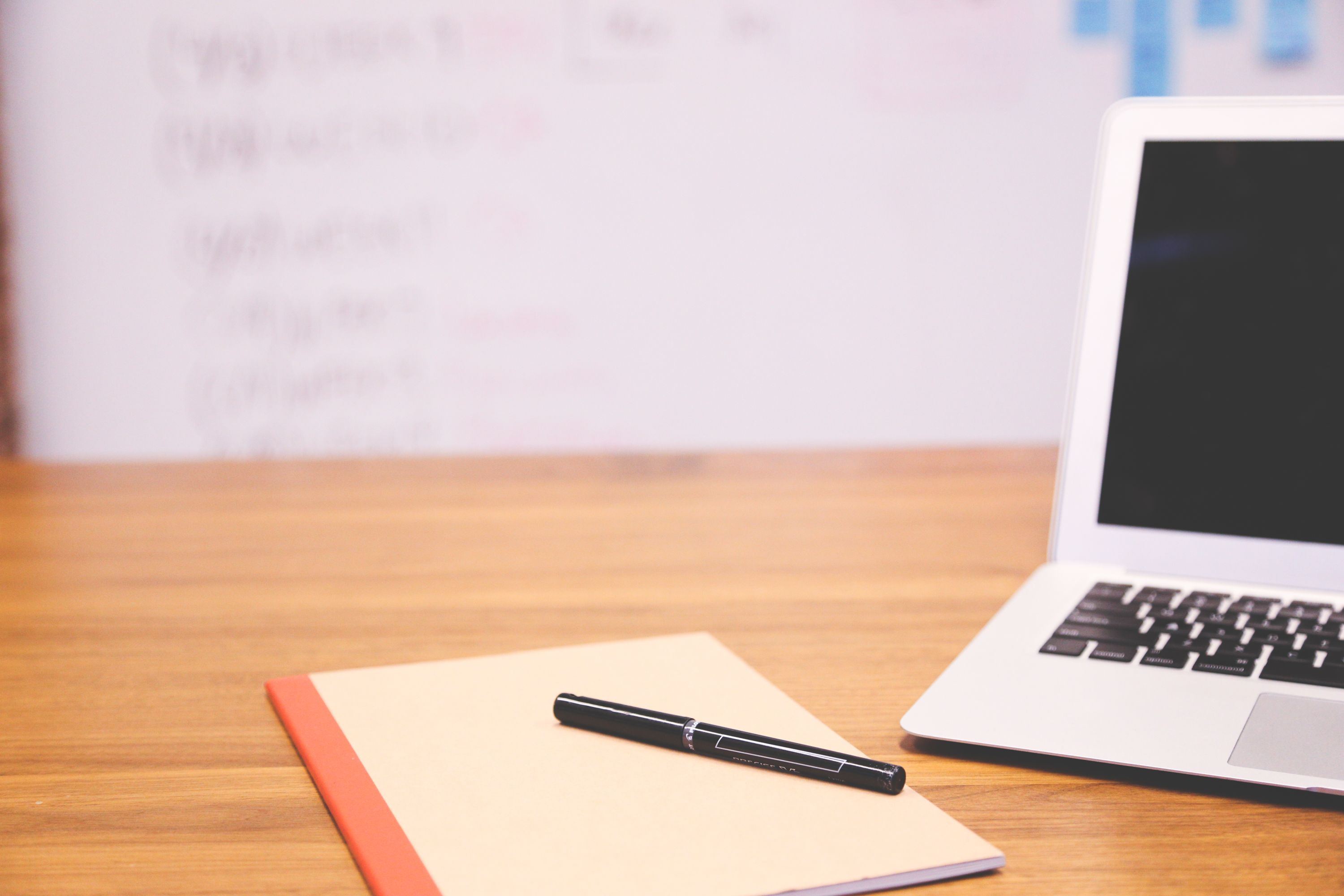 Laptop mit Tabellenkalkulation und offenem Notizbuch auf einem Schreibtisch
